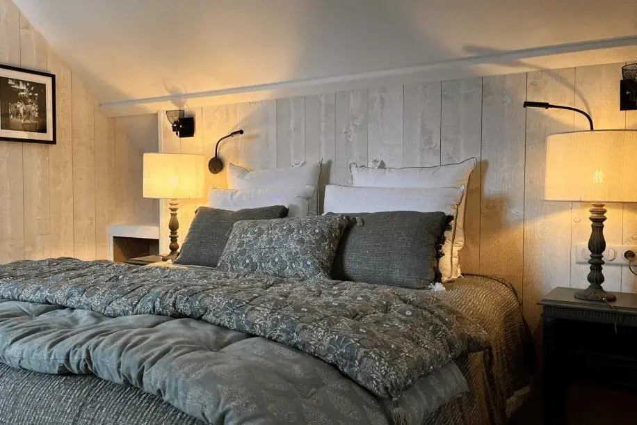 A cozy bedroom at La Plonplonière with a neatly made bed featuring grey and white bedding, two large pillows, and a wooden headboard—an inviting retreat in this charming Maison d'hôtes en Côte d'Opale.