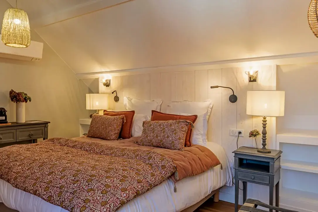 Cozy bedroom at La Plonplonière, a charming maison d'hôtes en Côte d'Opale, with a double bed featuring patterned bedding, bedside tables and lamps, wall-mounted reading lights, and warm ambient lighting for an inviting atmosphere.