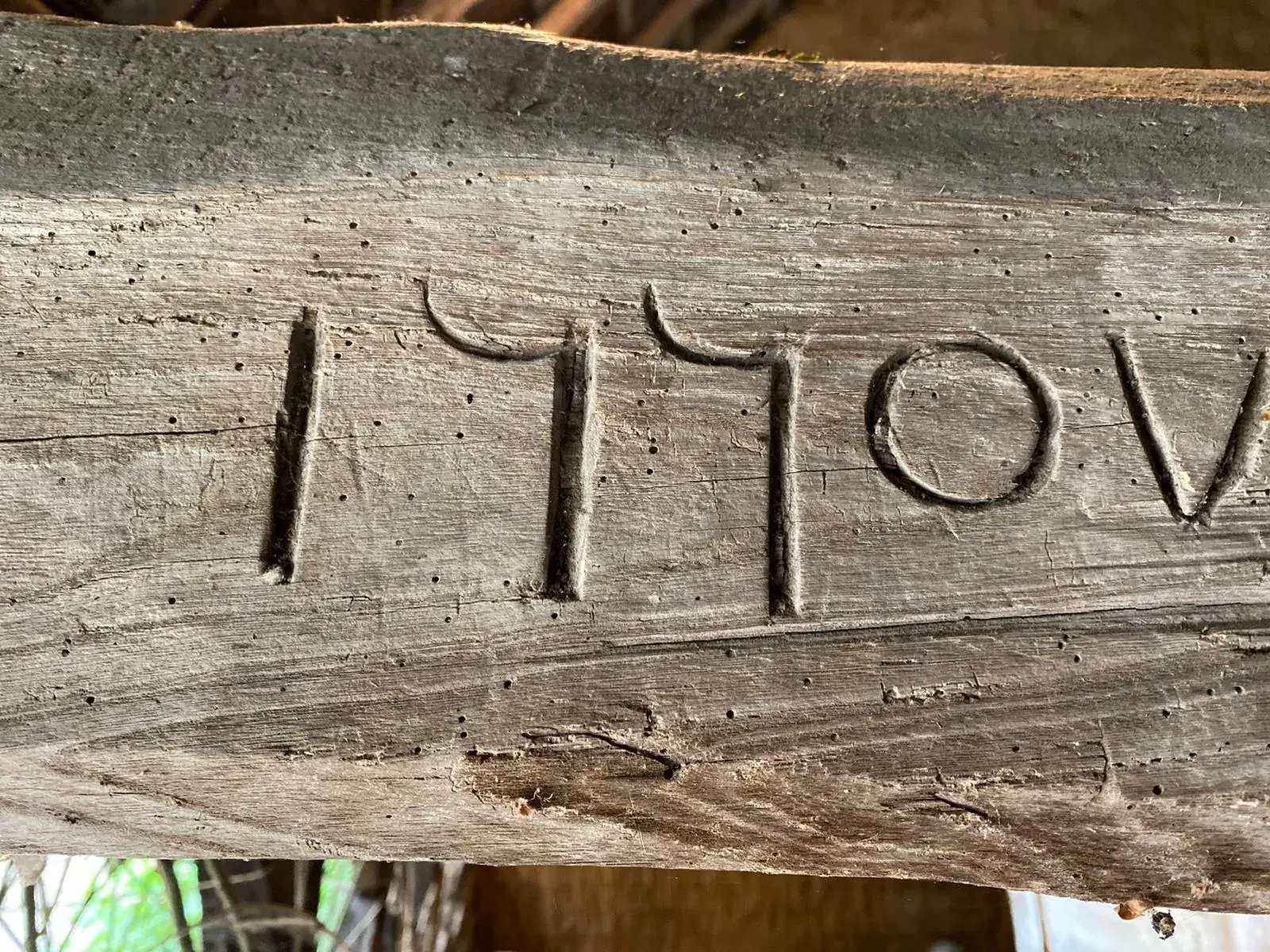 Close-up of a weathered wooden beam at La Plonplonière, Maison d'hôtes en Côte d'Opale, with the year 1770 carved in a stylized font. The rustic wood grain and age cracks evoke the region’s rich history and charm.