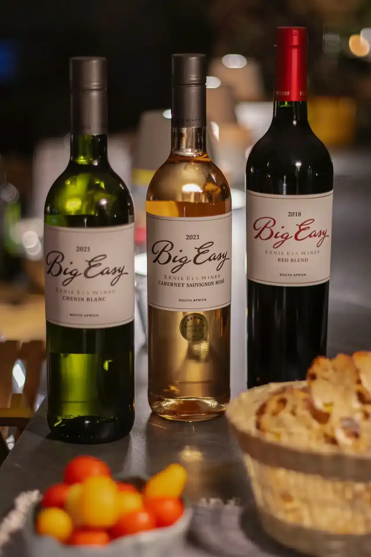 Three bottles of Big Easy wine—Chenin Blanc, Cabernet Sauvignon Rosé, and Red Blend—sit on a table beside bread and cherry tomatoes at La Plonplonière, charm-filled chambres d’hôtes en Côte d’Opale.