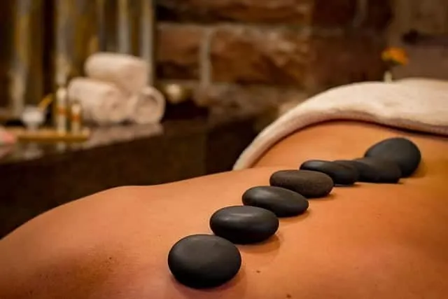 A person lies face down on a massage table at La Plonplonière, smooth black stones along their bare back in a tranquil spa setting—perfect relaxation at this Maison d'hôtes en Côte d'Opale. Rolled towels and a blurred background complete the scene.